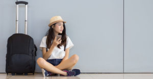 Asian woman teenager using smartphone at airport terminal sitting with luggage suitcase and backpack for travel in vacation summer relaxing waiting flight transport online check in or booking ticket