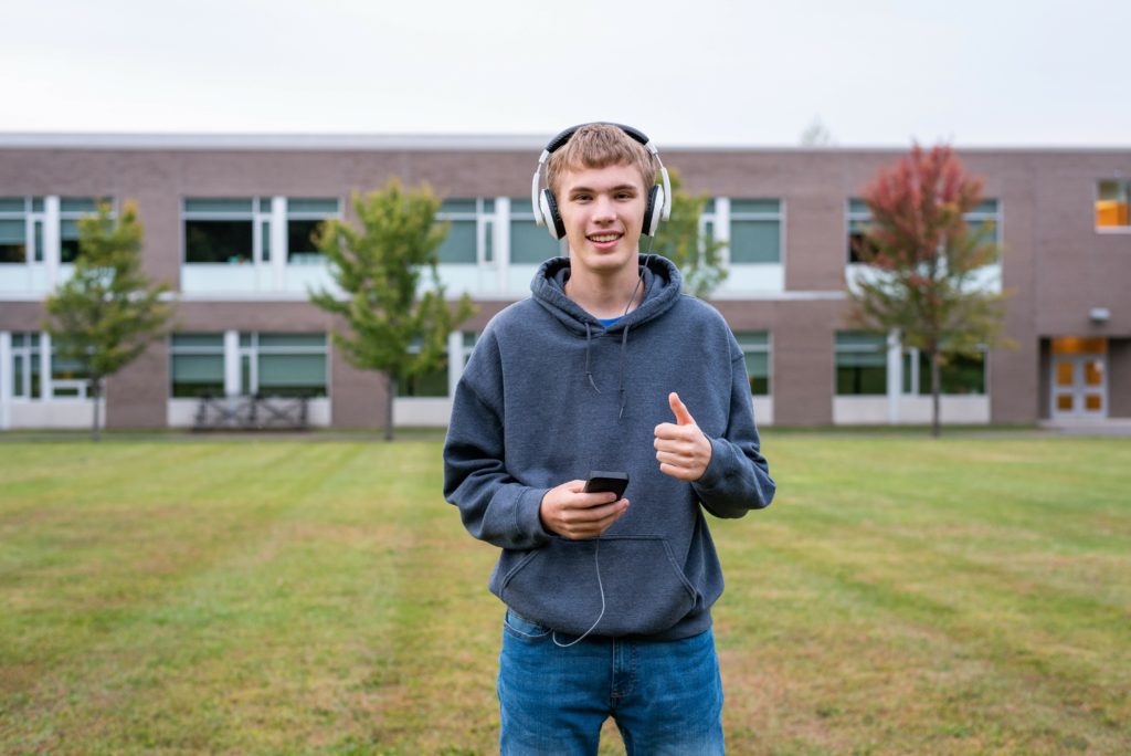 Happy teenager standing in the middle of a soccer field while listening to some music on an overcast day.